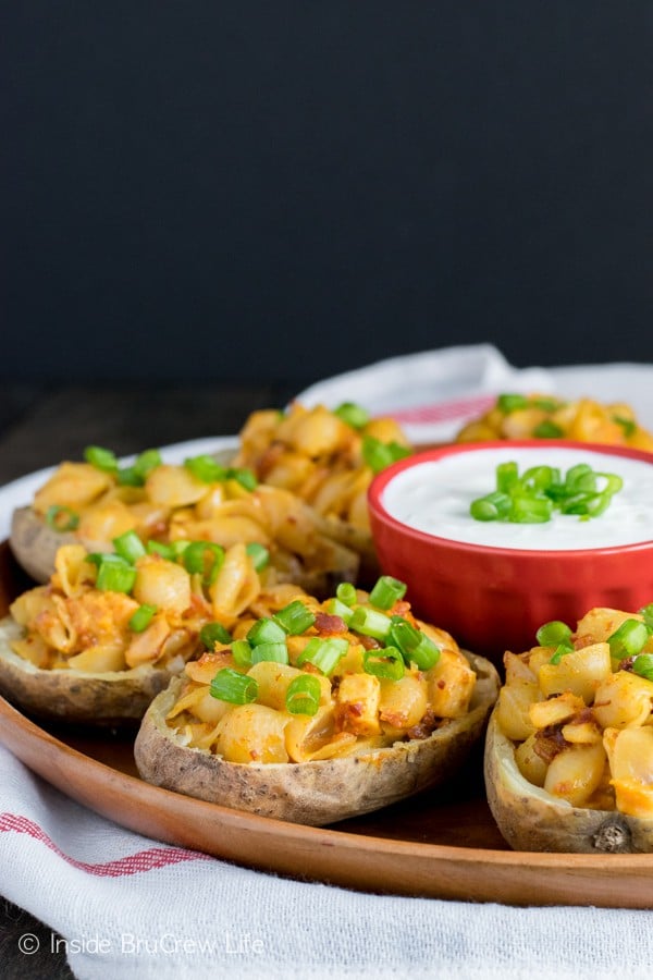 A wooden plate full of potato skins stuffed with spicy mac and cheese.