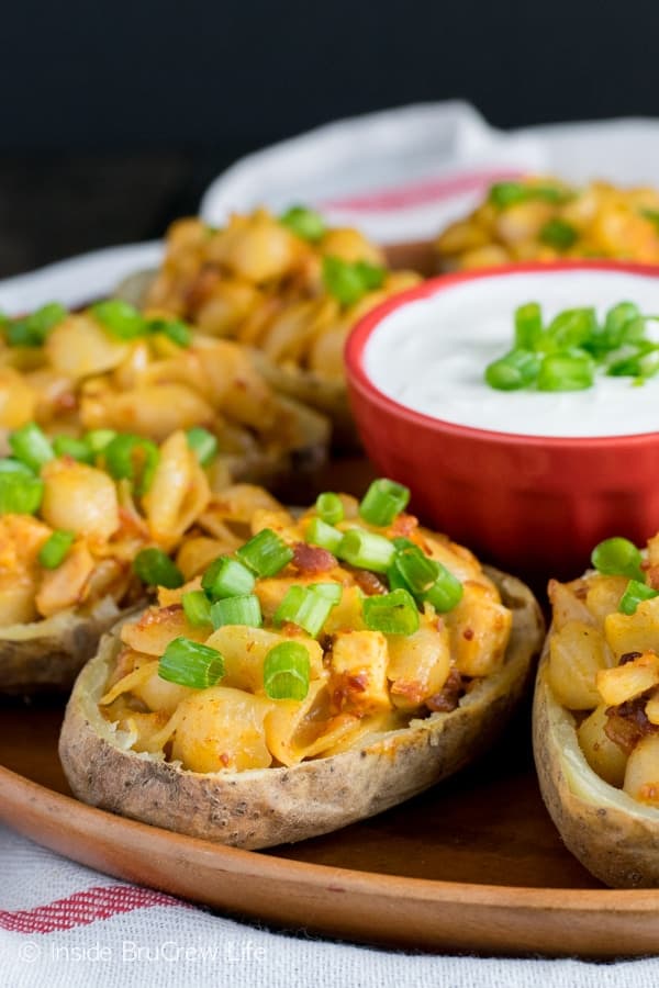 A wooden plate with potato skins stuffed with mac and cheese.