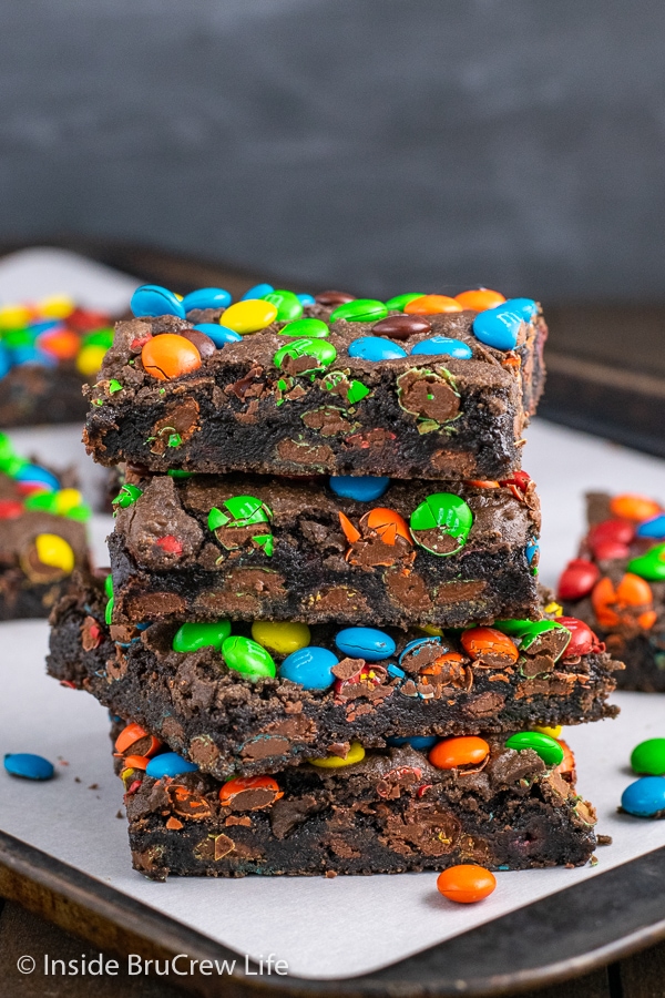 Four M&M's brownies stacked on top of each other on a tray with more brownies around it.