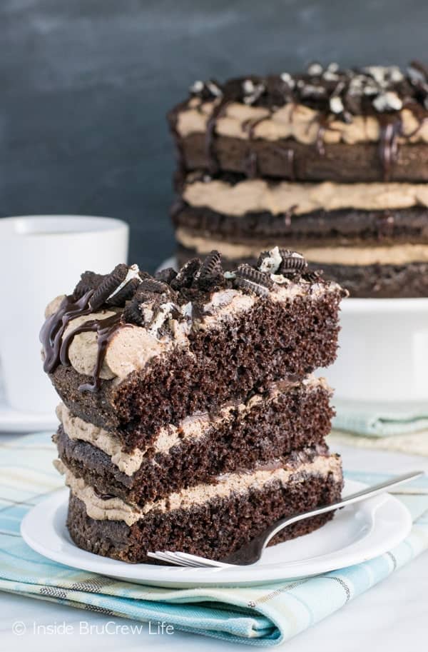 A white plate with a slice of mississippi mudslide cake topped with oreos and fudge and the rest of the cake behind it