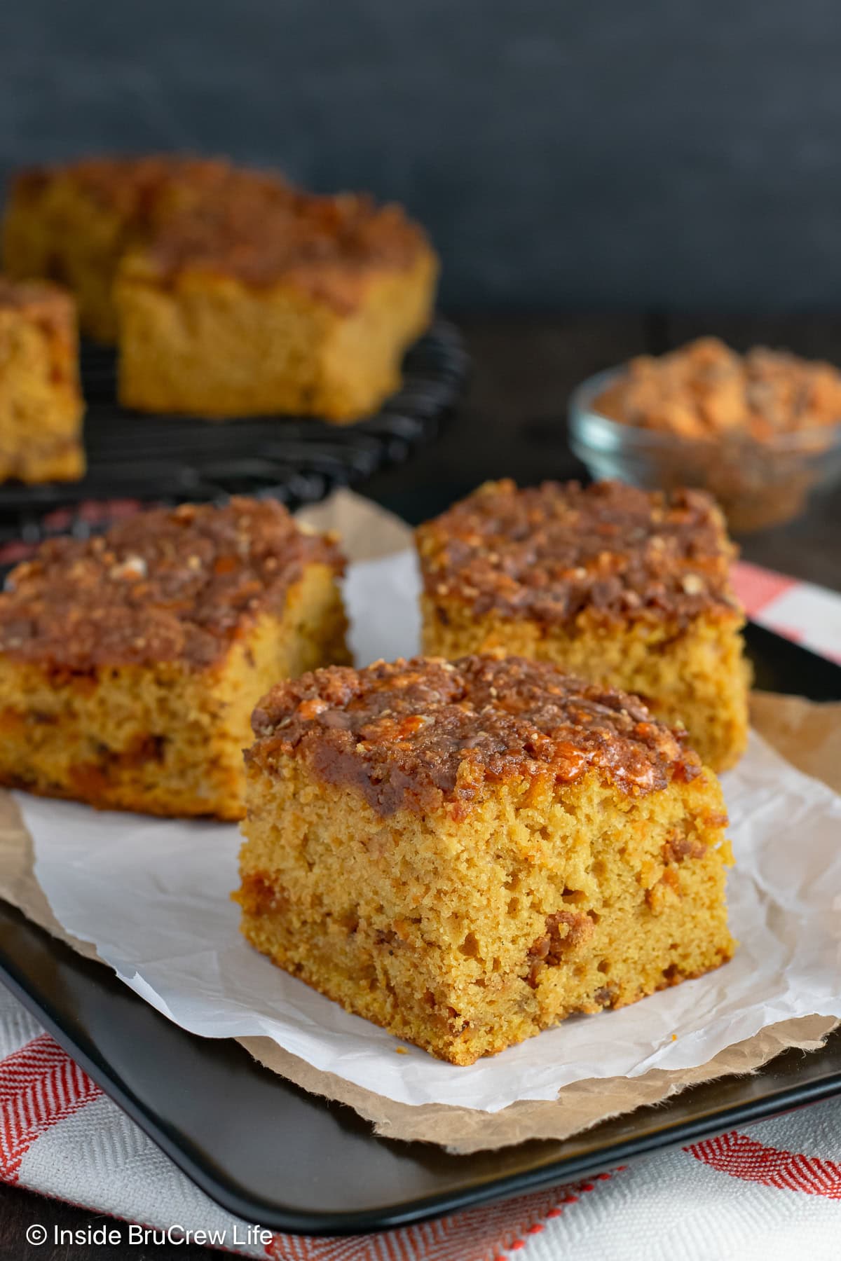 Squares of pumpkin cake with Butterfinger topping on a black plate.