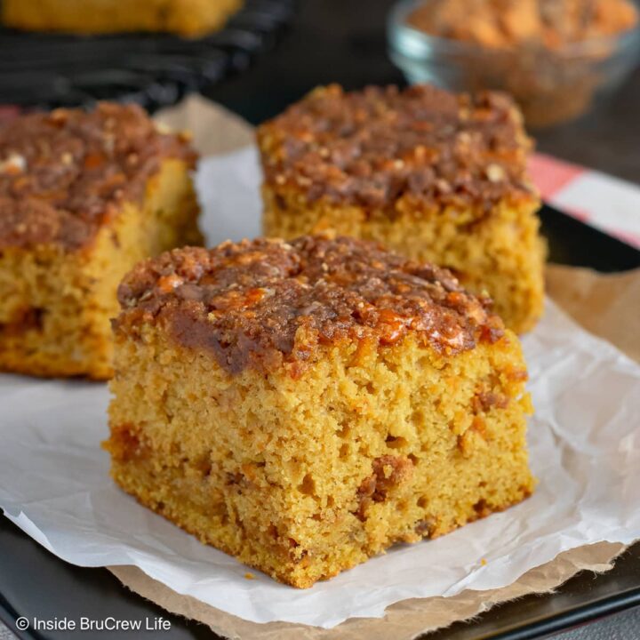 Squares of pumpkin cake with Butterfinger topping on a black plate.