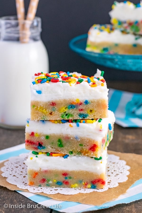 Three Funfetti Sugar Cookie Bars loaded with sprinkles and topped with vanilla frosting stacked on top of each other