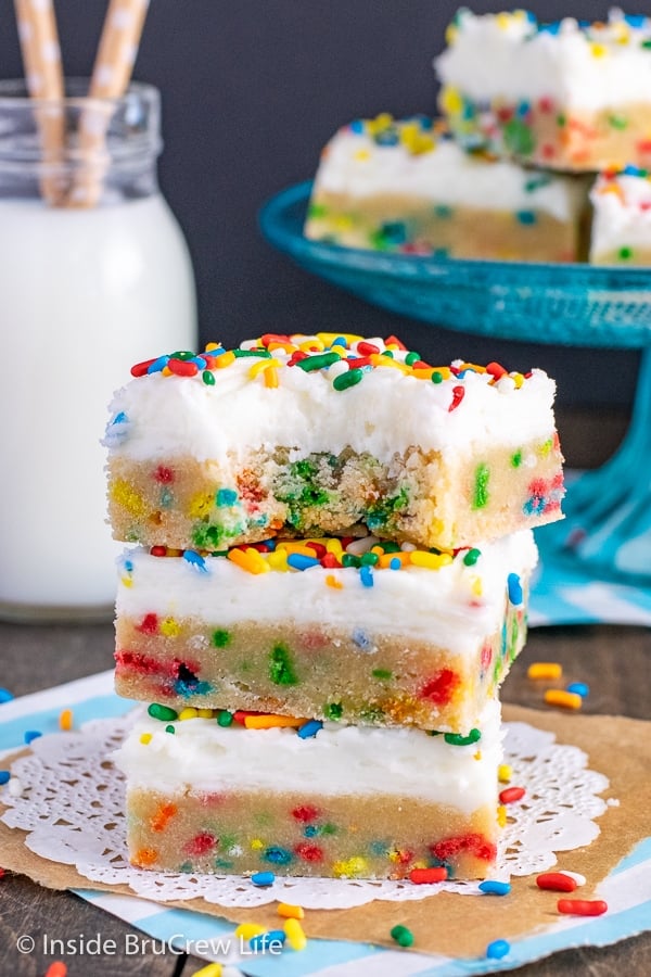 Three funfetti sugar cookie bars with vanilla buttercream frosting stacked on top of each other and a bite out of the top bar