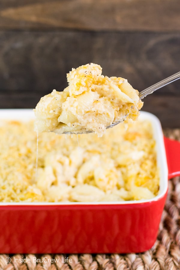 A red dish with three cheese macaroni and cheese in it and a spoon lifting a cheesy scoop out.