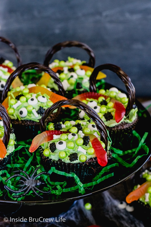 A black cake plate with brownie cupcakes topped with green frosting and spooky candies on it