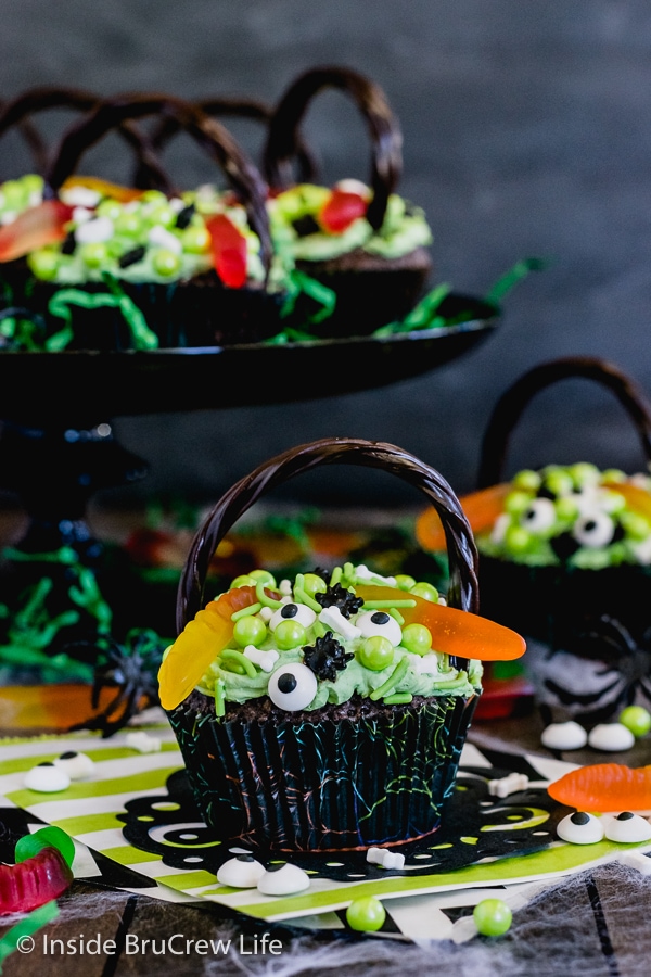 A brownie cupcake decorated with green frosting and spooky candies to look like a witch's cauldron with more cupcakes behind it