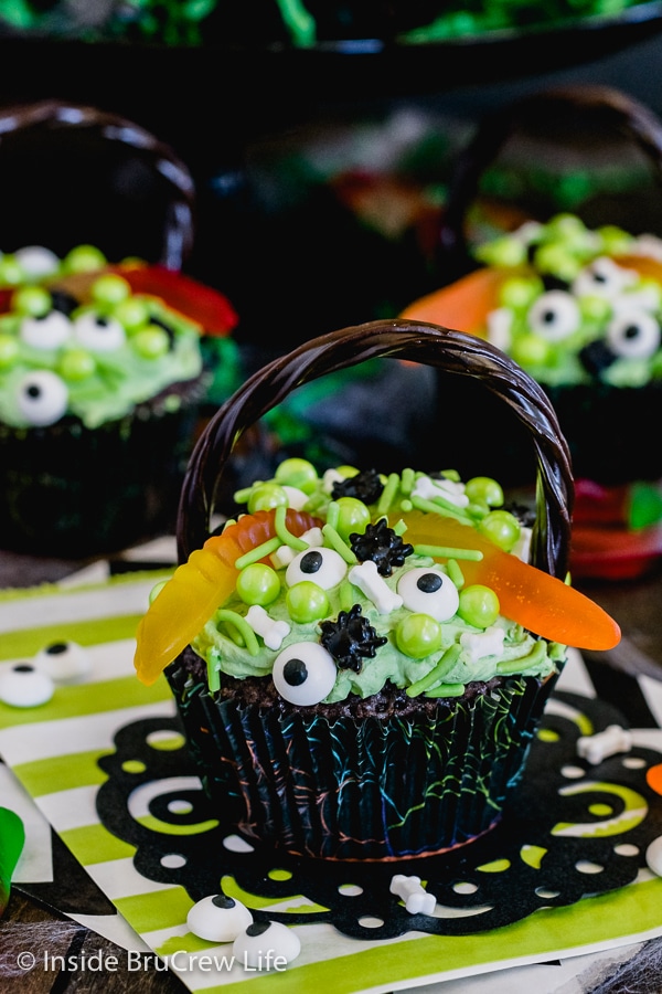 A close up picture of a brownie cupcakes topped with green frosting, gummy worms, and spooky sprinkles to look like a witch's cauldron