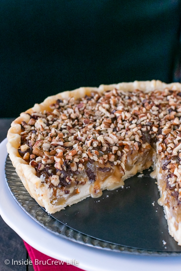 A white cake plate with a caramel apple tart on it missing a slice so you can see the dripping caramel inside.