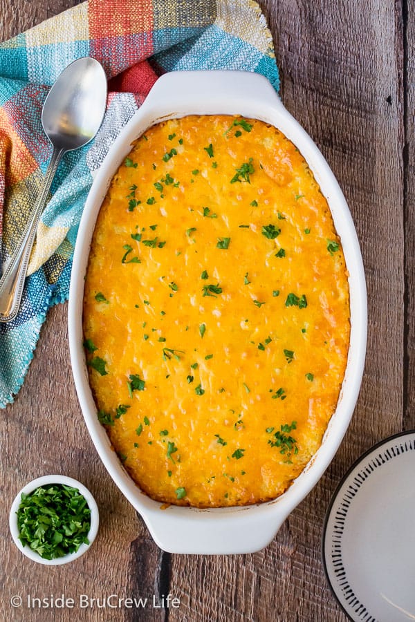 Overhead picture of a white casserole dish filled with cheesy hashbrown casserole on a wooden board.