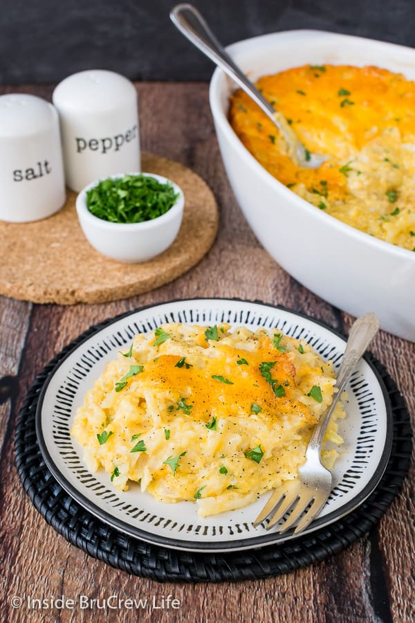 A white casserole dish with cheesy hashbrown casserole in it and a white plate with a serving of potatoes on it too.