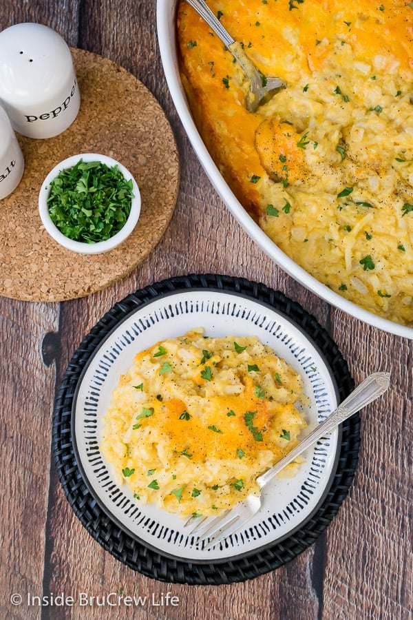 Overhead picture of a wooden board with a white dish full of cheesy potato casserole and a white plate with a serving of potatoes on it.