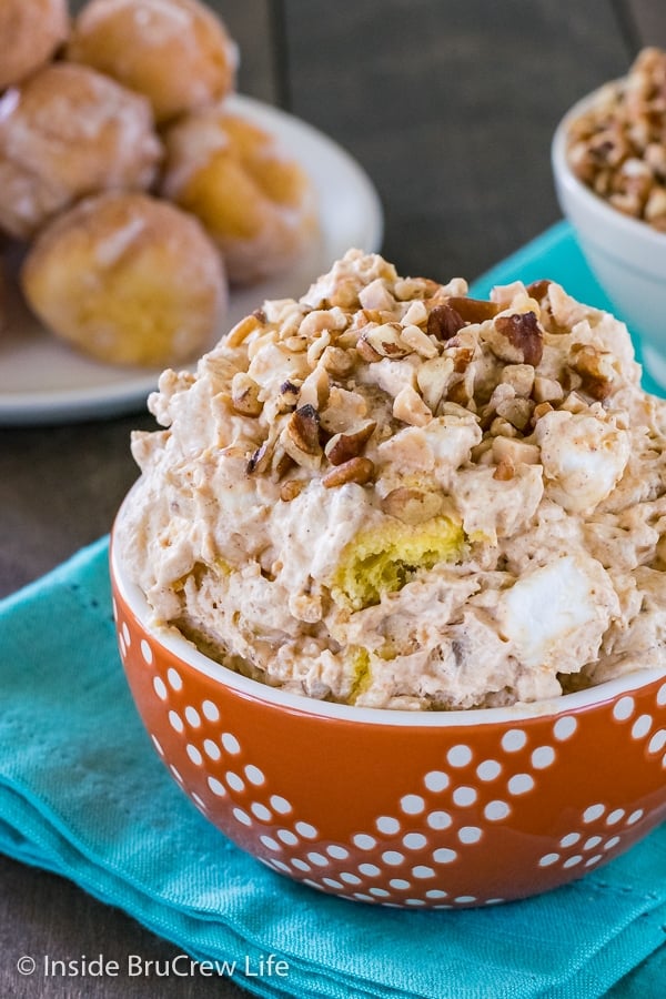 A close up of an orange bowl filled with pumpkin fluff salad with nuts and toffee on top