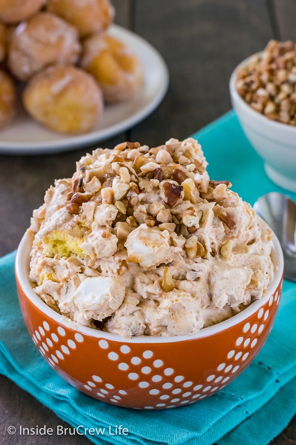 An orange bowl on a teal towel filled with pumpkin fluff salad and topped with nuts and toffee