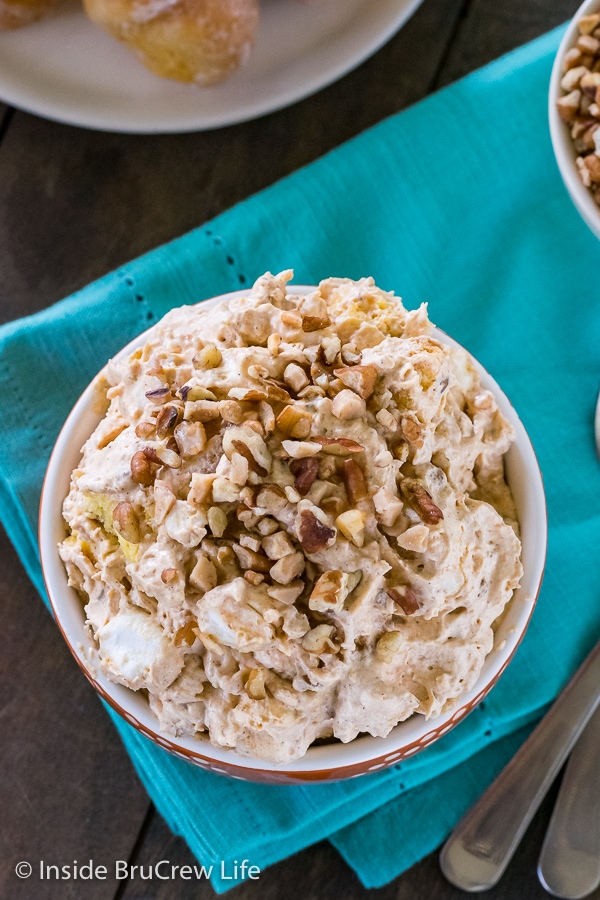 Overhead picture of a bowl on a blue towel filled with pumpkin fluff salad and topped with nuts and toffee