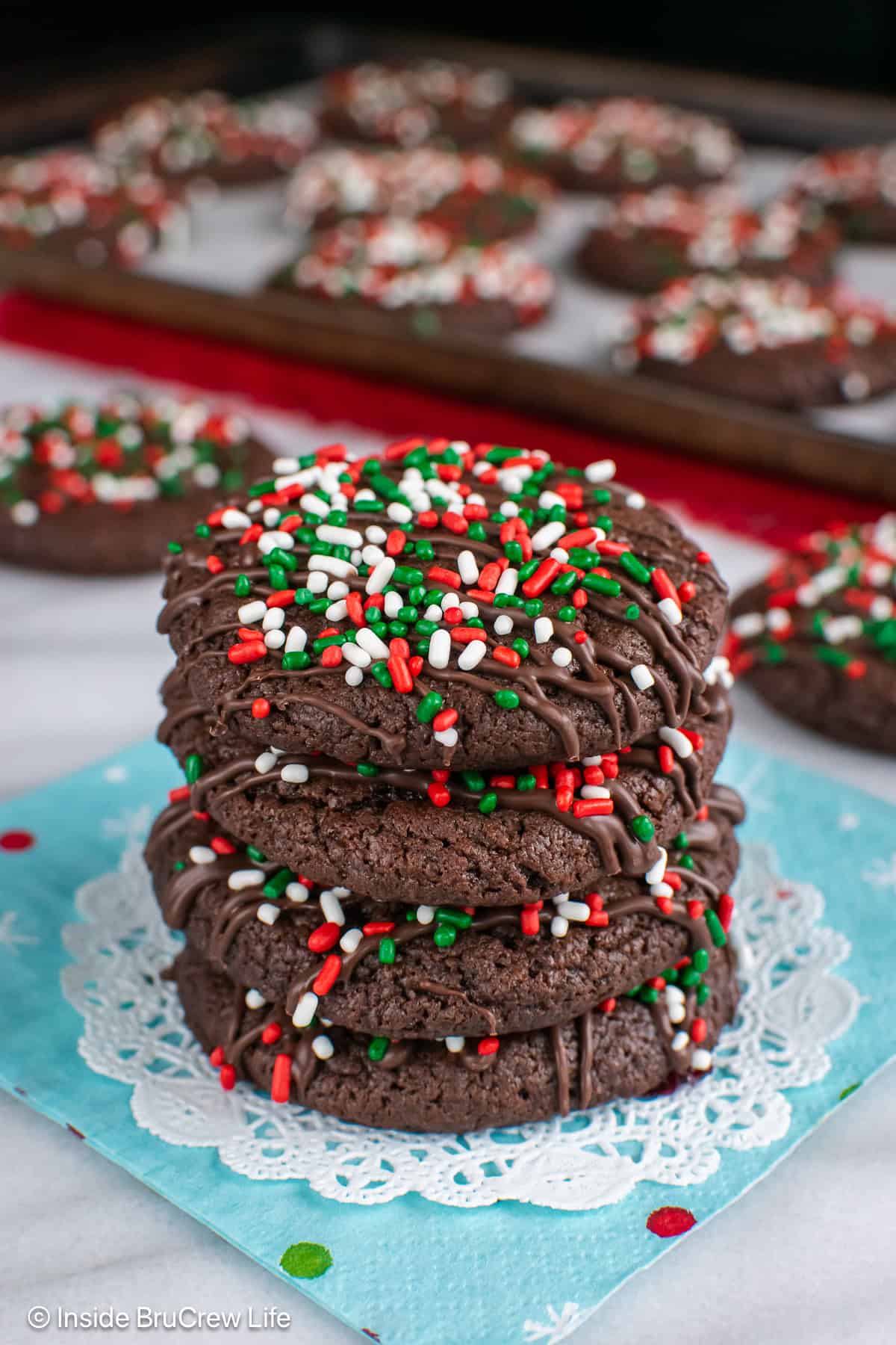 Four chocolate cake mix cookies decorated with Christmas sprinkles stacked in a pile.
