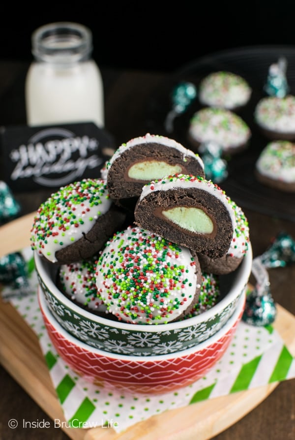 A green and red bowl filled with chocolate mint snowball cookies that are dipped in white chocolate and have sprinkles on top