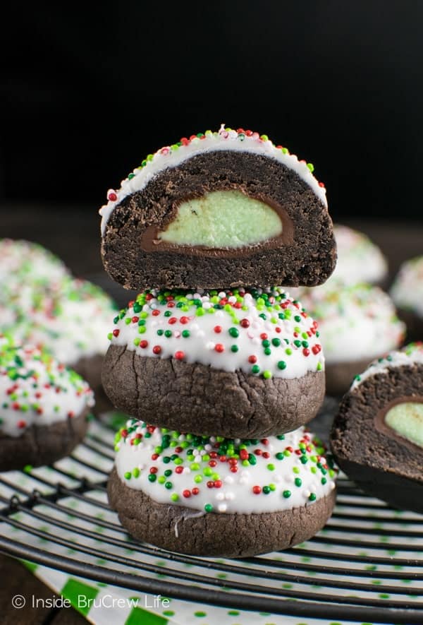 Stack of three chocolate mint truffle snowball cookies on a black wire rack with the top cookie cut in half to show the hidden kiss
