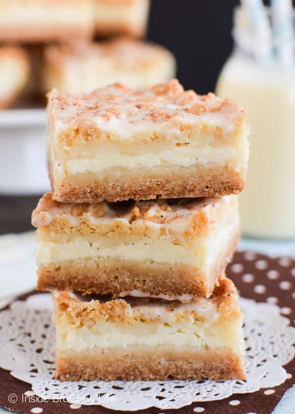 A stack of three eggnog cheesecake bars on a white doily with a glass of eggnog behind it