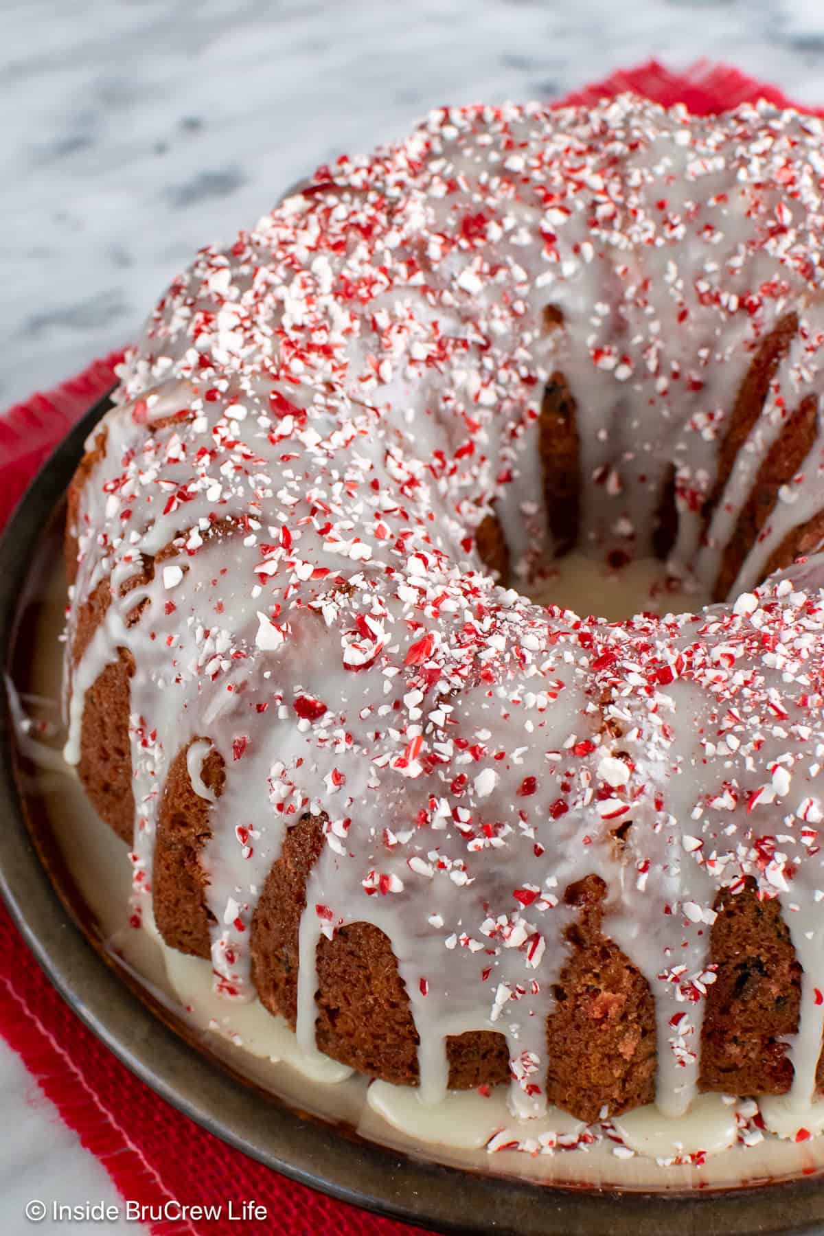 A glazed peppermint cake on a cake topped with candy crunch pieces.