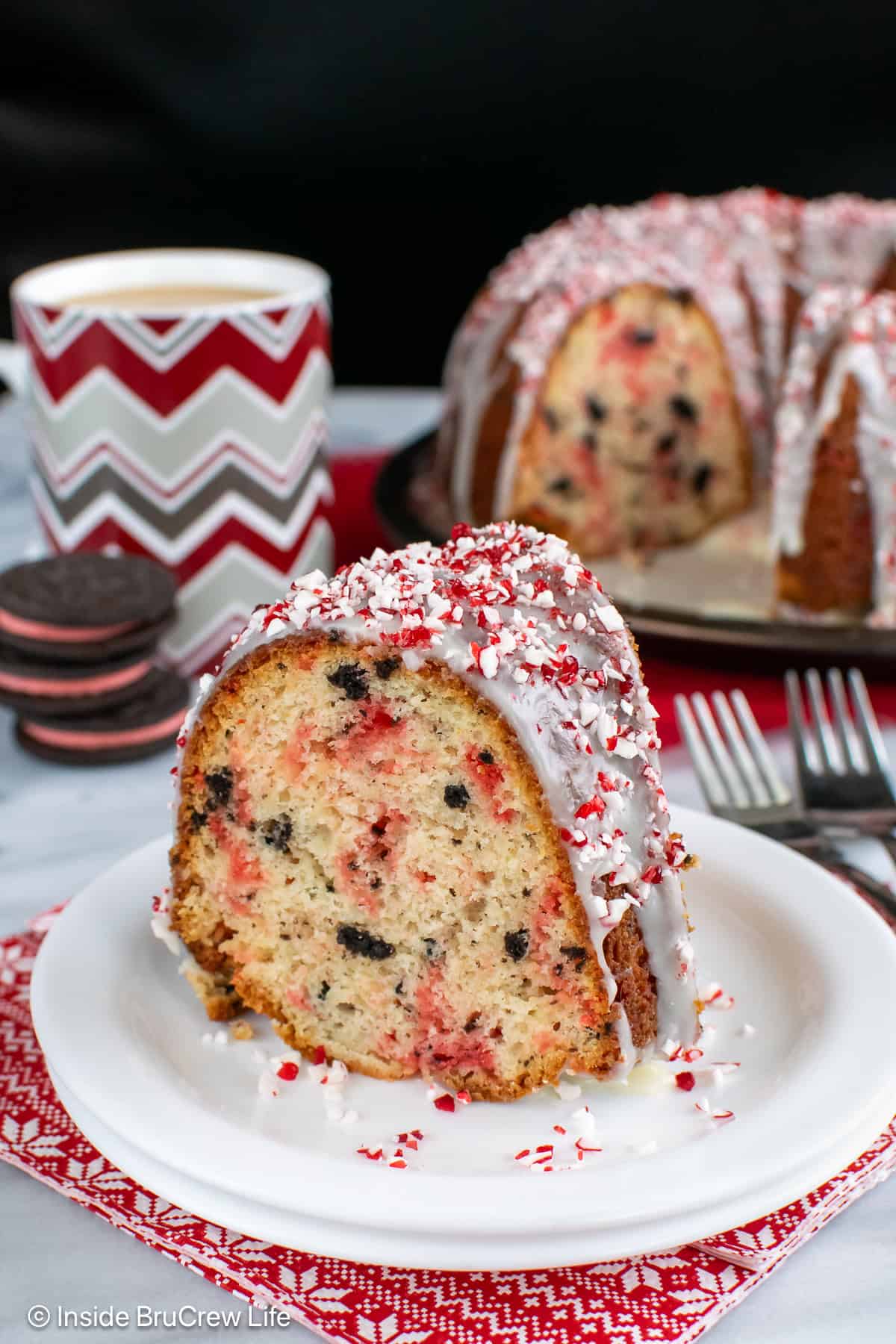 A slice of peppermint oreo cake on a plate with the rest of the cake behind it.