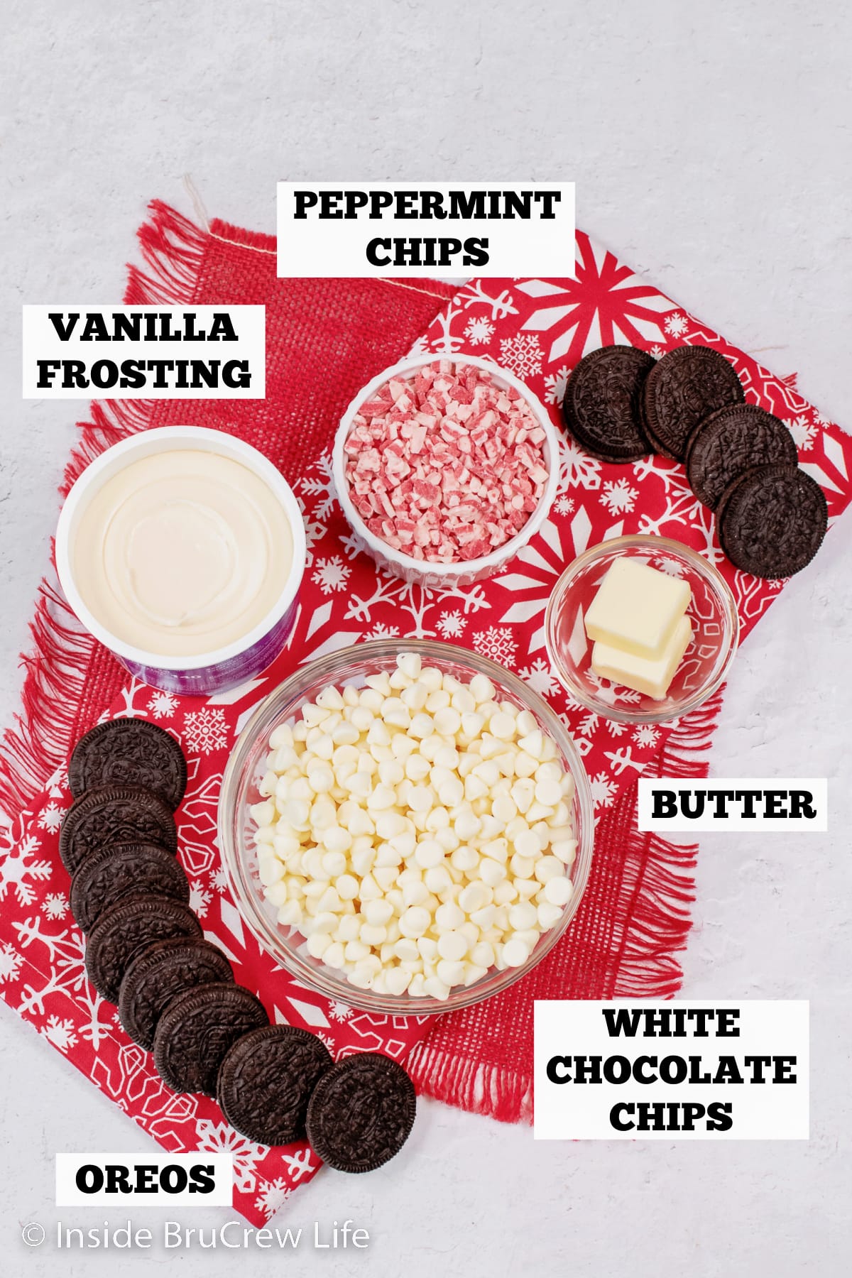A white board with bowls of ingredients for peppermint Oreo fudge.