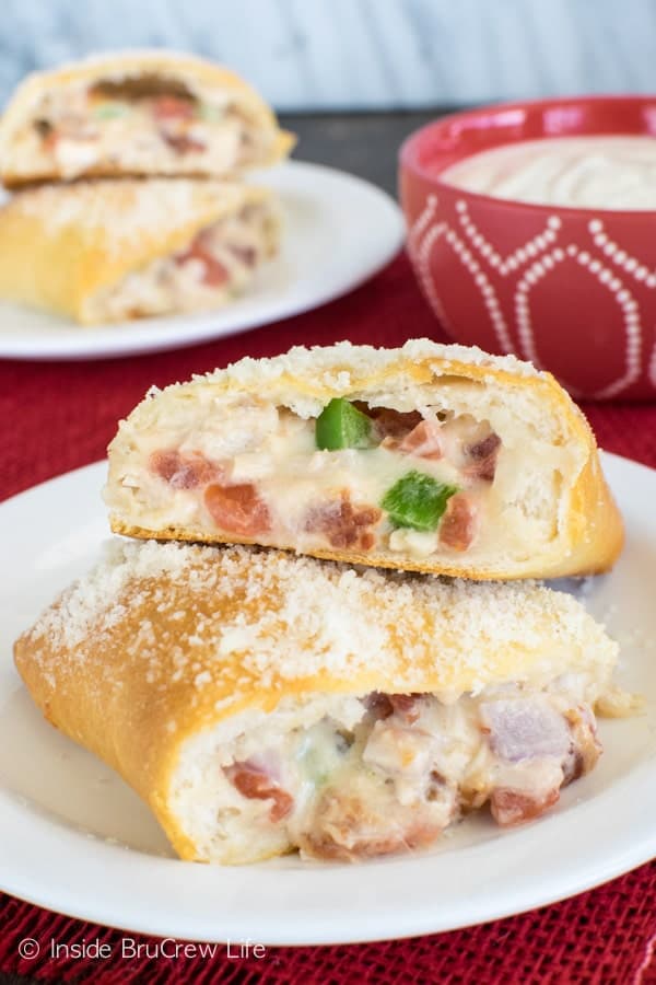 A Chicken Alfredo Calzone cut in half and stacked on top of each other on a white plate showing the cheesy middle