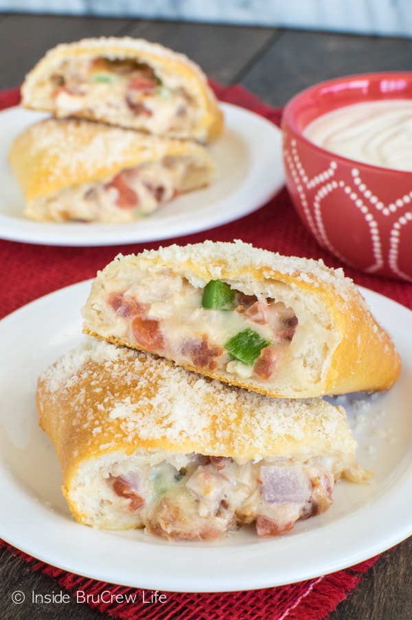 A chicken alfredo calzone cut in half and stacked on a white plate showing the cheesy center