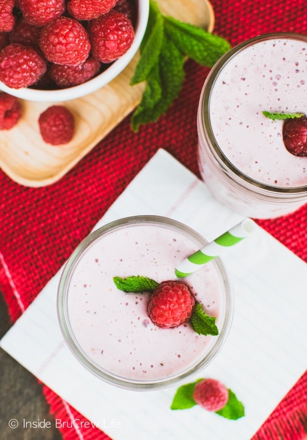 An overhead picture of a pink smoothie in a clear mason jar with a raspberry, mint leaf, and green and white straw in it.