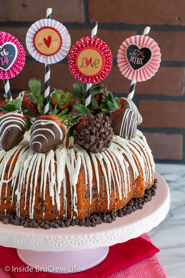 Close up of full Strawberry Chocolate Chip Bundt Cake with white chocolate drizzles on a pink cake plate