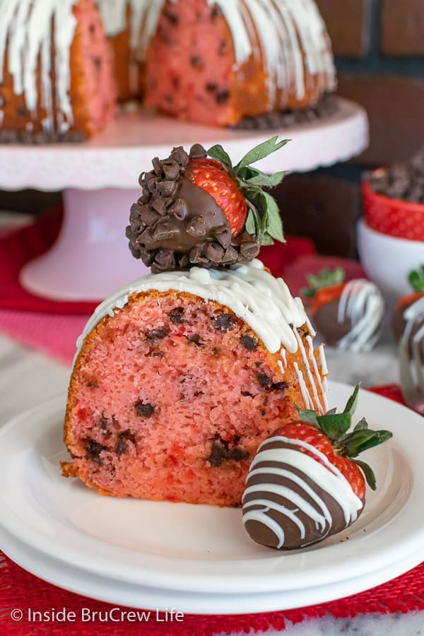 A slice of Strawberry Bundt Cake with chocolate chips on a white plate with chocolate covered strawberries