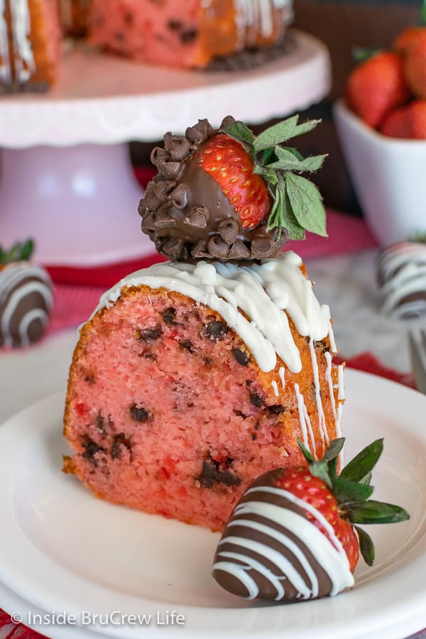 Close up of slice of strawberry chocolate chip bundt cake with chocolate covered strawberries