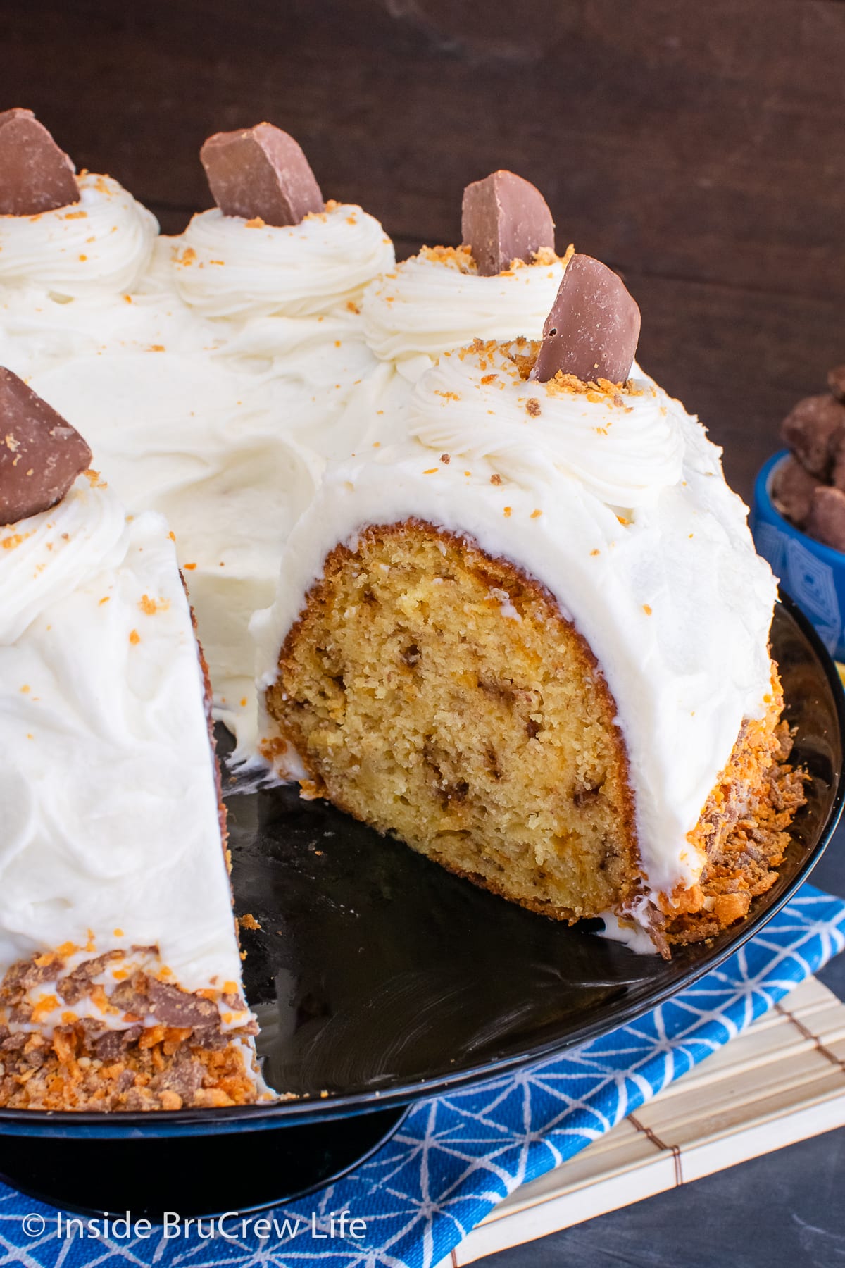 A frosted banana cake on a black cake plate.