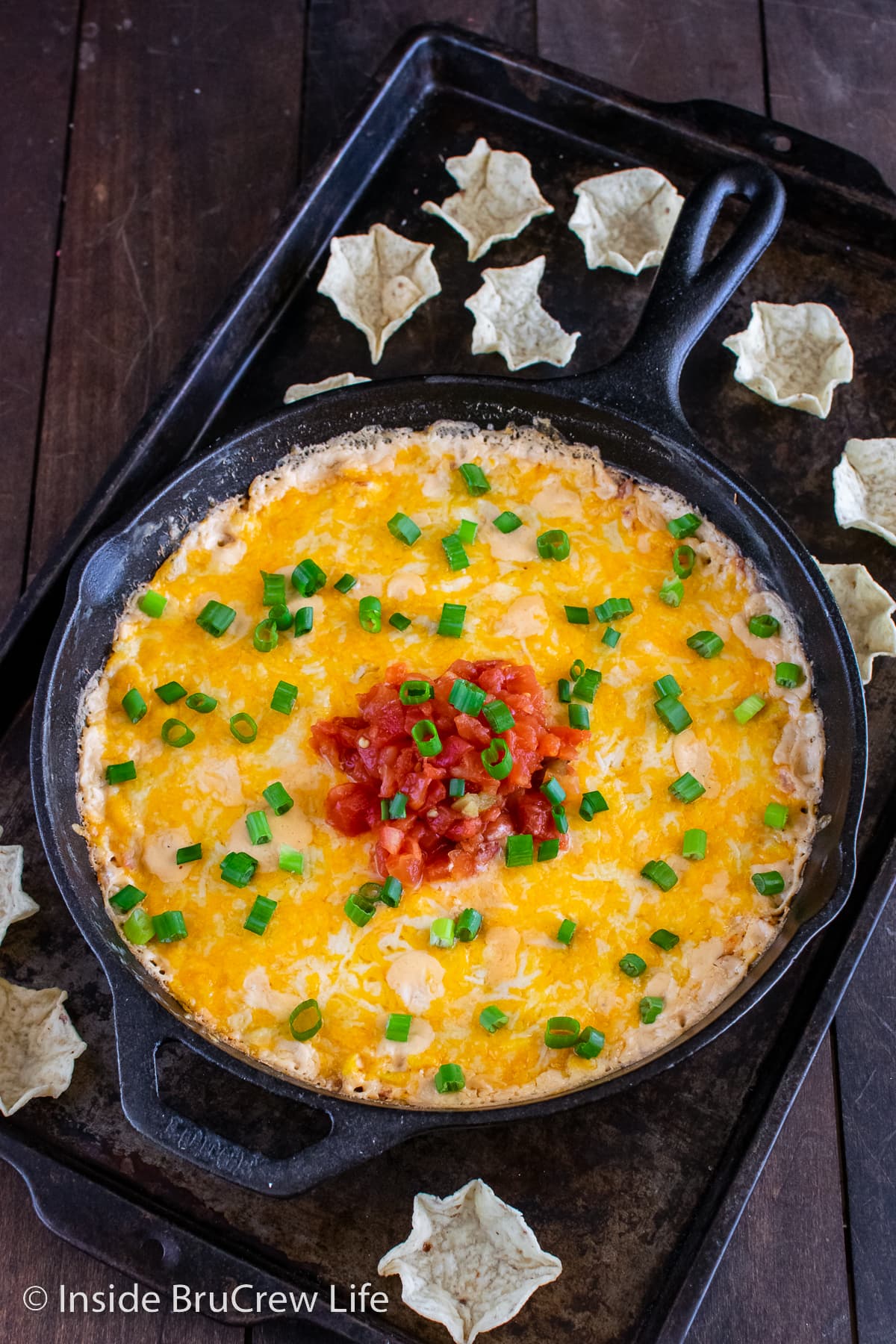 A black skillet filled with a cheesy corn dip.