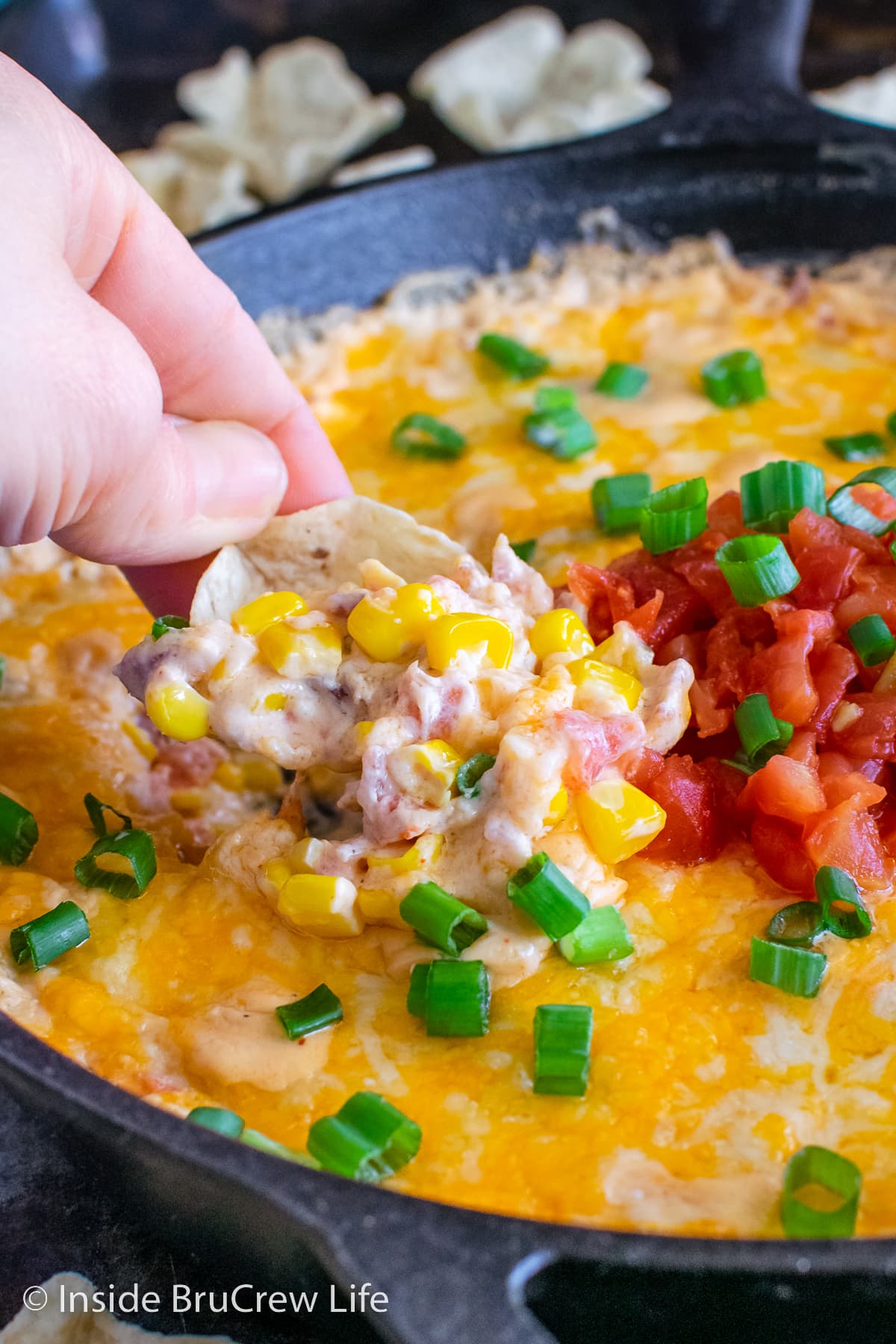 A chip digging into a cheesy corn dip.