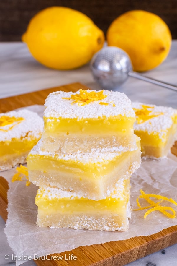 A stack of three lemon squares with powdered sugar on a wooden board.