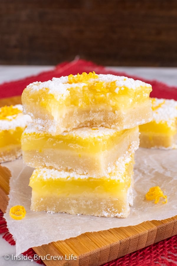 Three lemon bars stacked on top of each other with a bite taken out of the top bar