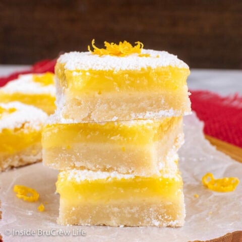 Three lemon bars with powdered sugar stacked on top of each other on parchment paper