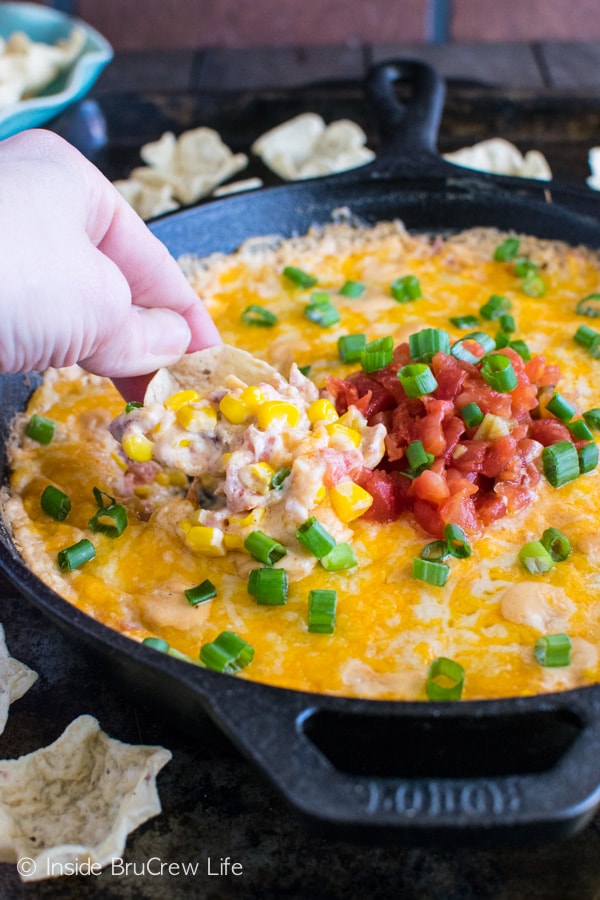 A chip scooping hot corn dip out of a cast iron pan.
