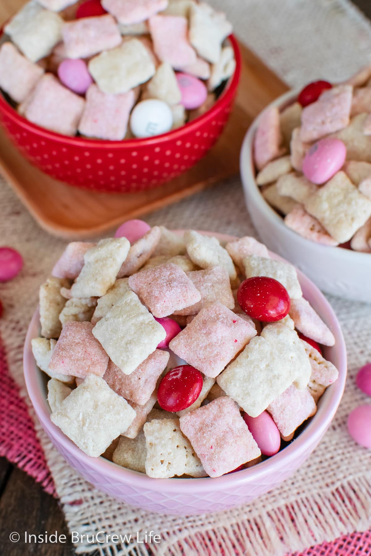 Bowls filled with strawberry chex mix on a pink towel.