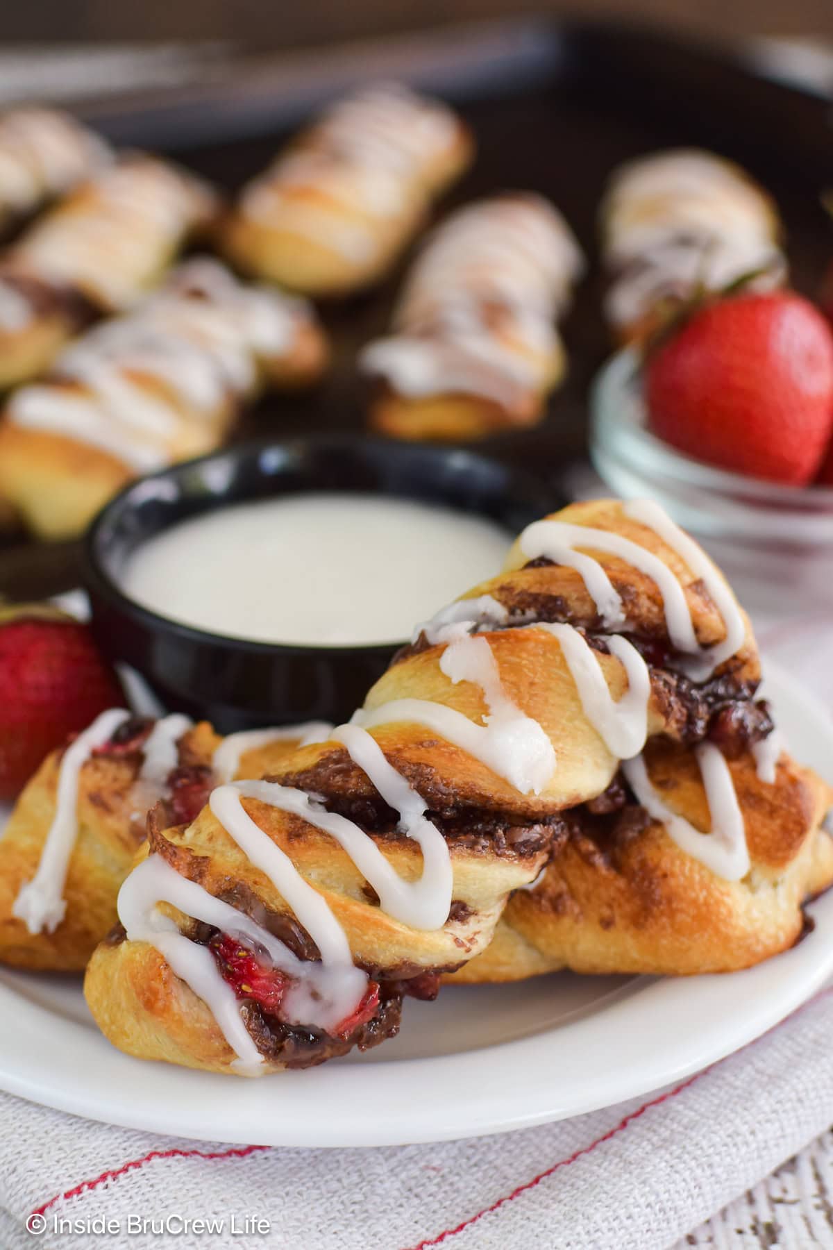 Pastry twists on a white plate with a bowl of frosting.