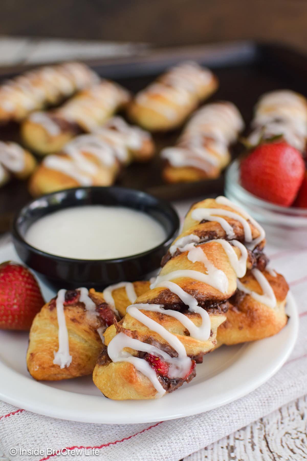 Two nutella twists stacked on a plate with a bowl of frosting.