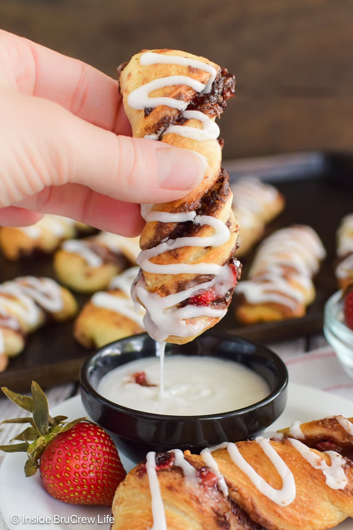 A nutella pastry roll being held and dipped into a bowl of frosting.