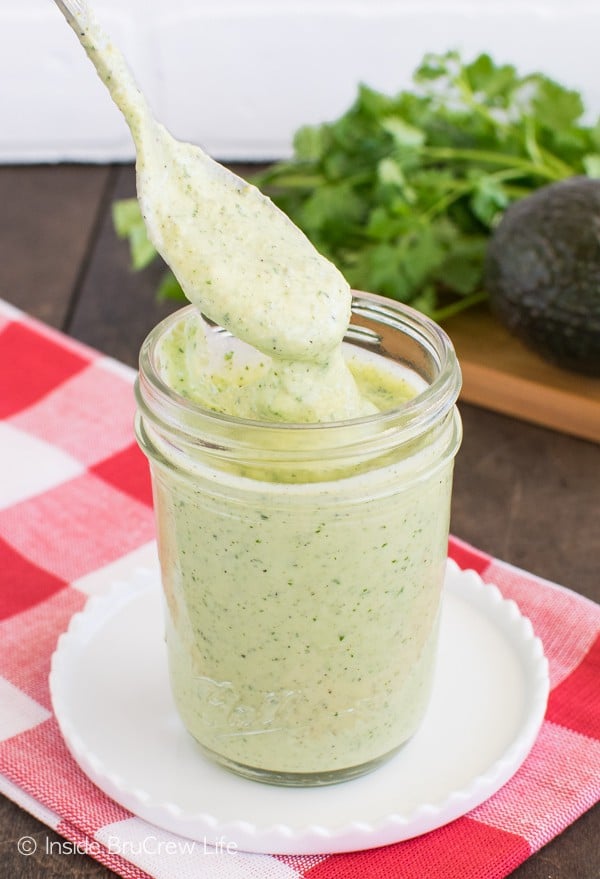 A clear Mason jar filled with avocado salad dressing with a spoon lifting dressing out of the top.