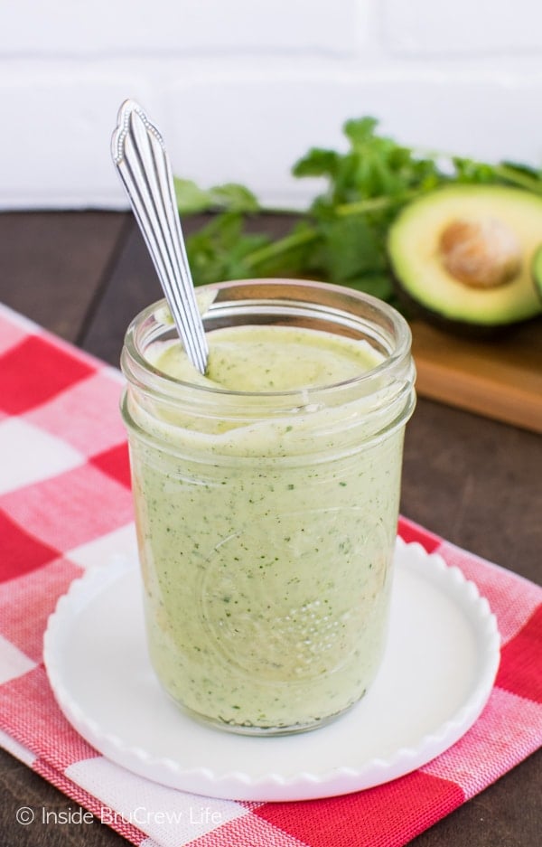 A clear Mason jar on a white plate filled with a green avocado lime sauce.