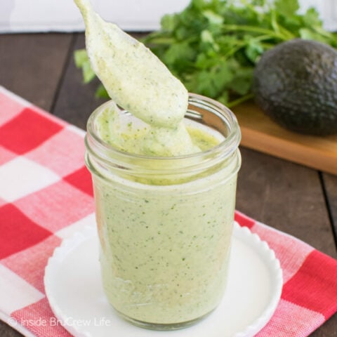 A clear mason jar filled with avocado salad dressing and a spoon lifting some out.