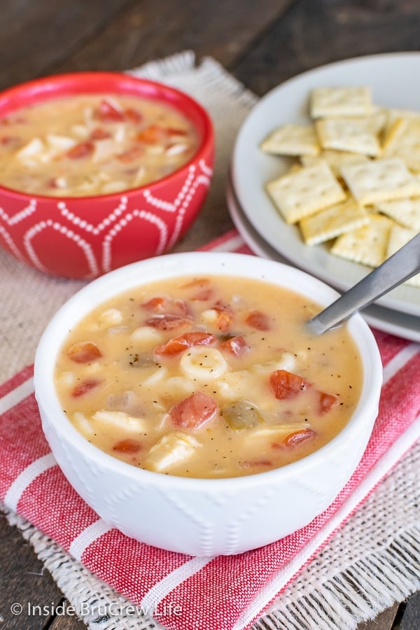 Two bowls filled with cheesy chicken soup and a plate of crackers behind them