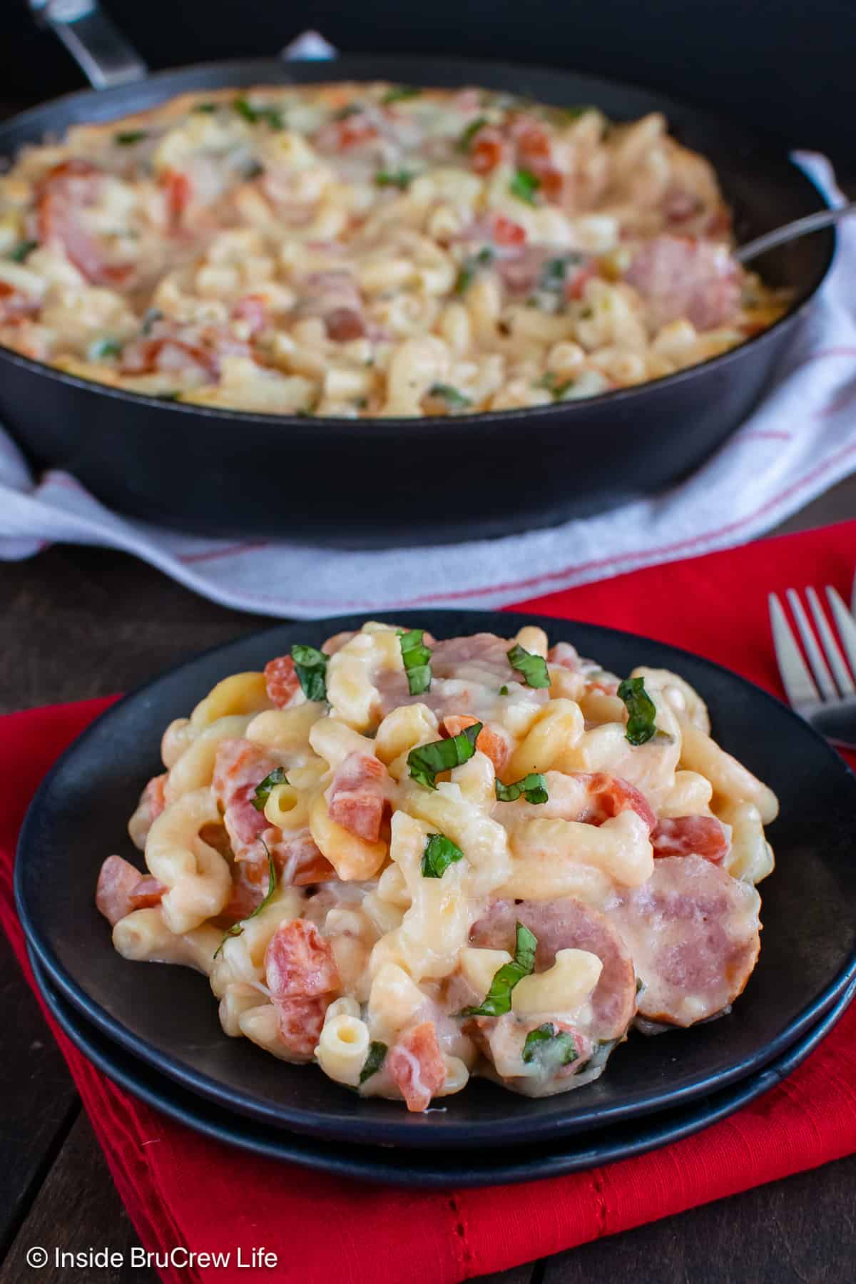 A black plate with a serving of cheesy smoked sausage pasta.