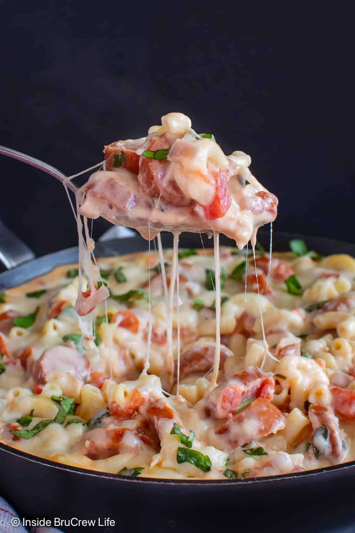 A spoonful of cheesy pasta being lifted out of a skillet.