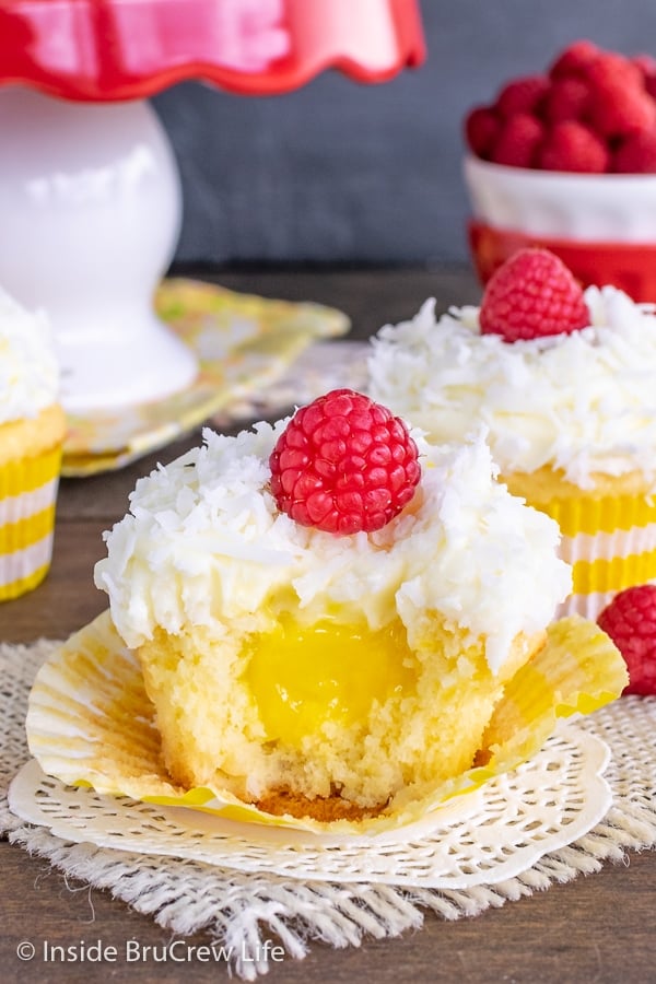 A coconut cupcake with lemon frosting and a raspberry with a bite taken out showing the hidden lemon pie filling center.